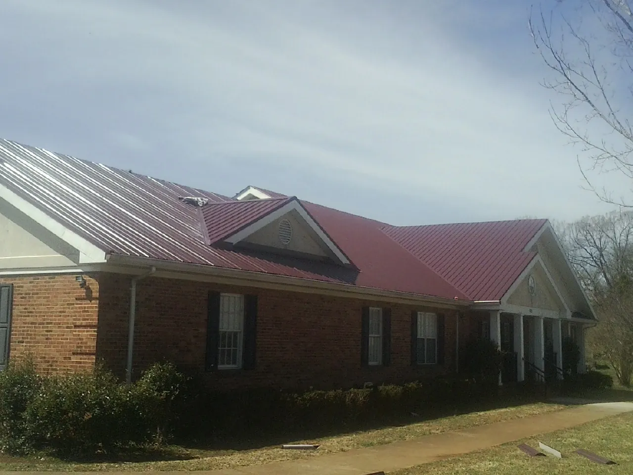 Red metal roof with gabled entries on a long brick building, from a Hail Damage Roof Repair job in Litchfield Park