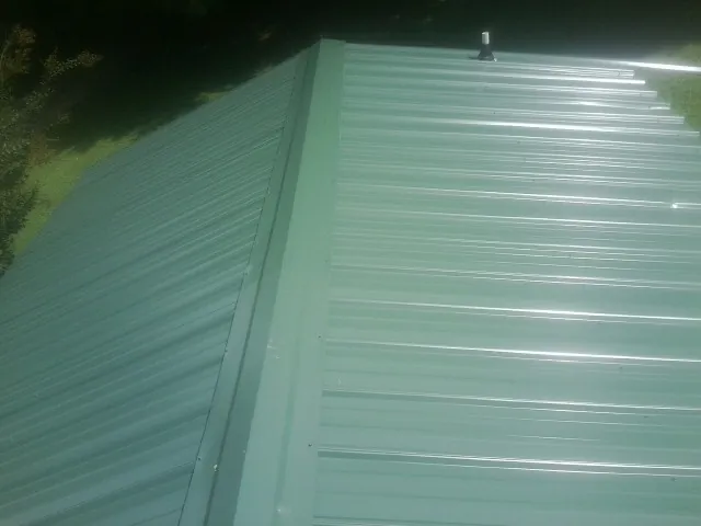 New green metal panels meeting at the ridge of a roof — Flat Roof Repair work by our crew in Litchfield Park