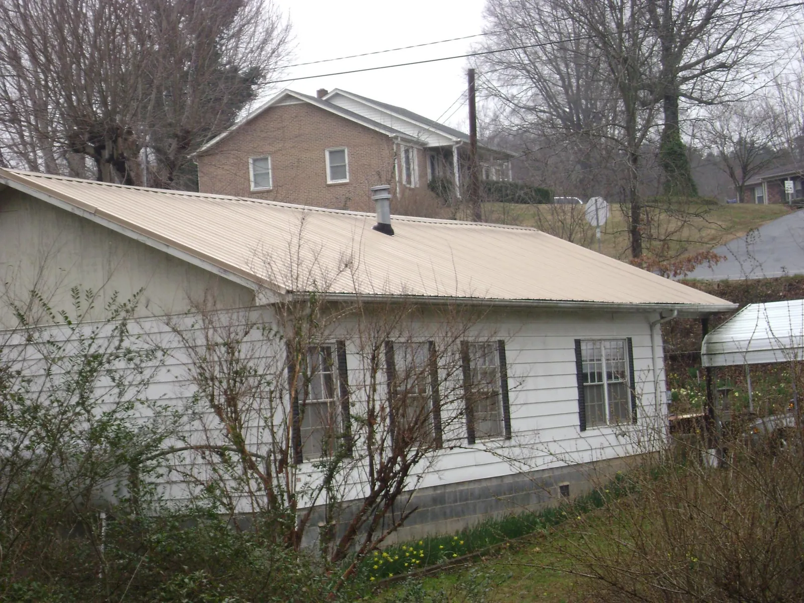 Tan metal roof on a white sided house set into a hillside — Commercial Roofing by Roofing Brothers in Litchfield Park